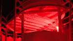 A winterover standing in the dark, under red light, near a somewhat tall snowdrift at the station entrance.