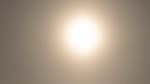 Bright moon with halo in gray sky over gray, barren landscape.