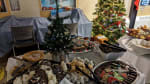 A table loaded with trays of cookies and treats, decorated Christmas tree in background.