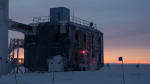 Orange light along the horizon before sunrise at the South Pole, IceCube Lab in foreground.
