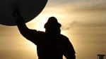 Shadow view of person standing and blocking sun behind them, holding a large weather balloon overhead.