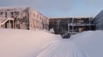 Tall snowdrifts lining a path facing the back of the South Pole station.