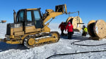Heavy machinery and a few workers out on ice under clear skies.