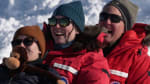 Three people on a sled, smiling, as they reach the bottom of the hill.
