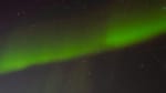 Bright green streak of aurora spreading as diagonal line across full star-studded sky.