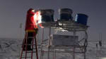 Winterover on a ladder with a lamp removing covers from a trio of field telescopes.