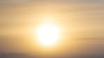 Large, bright sun low in the sky at the South Pole, with some wispy clouds and two people walking together in the distance.