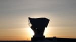Sunrise at South Pole, with low sun directly behind South Pole Telescope, leaving surroundings in dark and shadow.