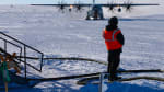 An aircraft marshaller seen from behind, waiting as large turboprop plane approaches.