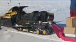 Person with arms up, standing on top of bundles of trash piled on long sled.