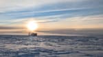 A bright sun low in a mostly cloudy sky above the IceCube Lab.