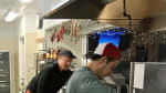 Side view of several people working at different stations of industrial kitchen.