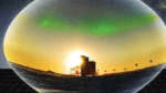 A South Pole scene of the IceCube Laboratory against a backdrop of auroras displayed inside an artistic rendition of a photomultiplier tube.