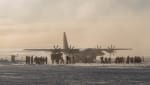 Group of people boarding a large plane in the distance on the ice at the South Pole under somewhat hazy sky.