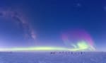 View of the ceremonial South Pole, with its circle of flags, underneath the Milky Way and a swath of auroras.