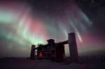 Multicolored auroras fanning out across sky above IceCube Lab, in full shadow.
