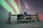 The IceCube Lab with a pseudo-split-screen background of Milky Way and stars off to the right and auroras off to the left.