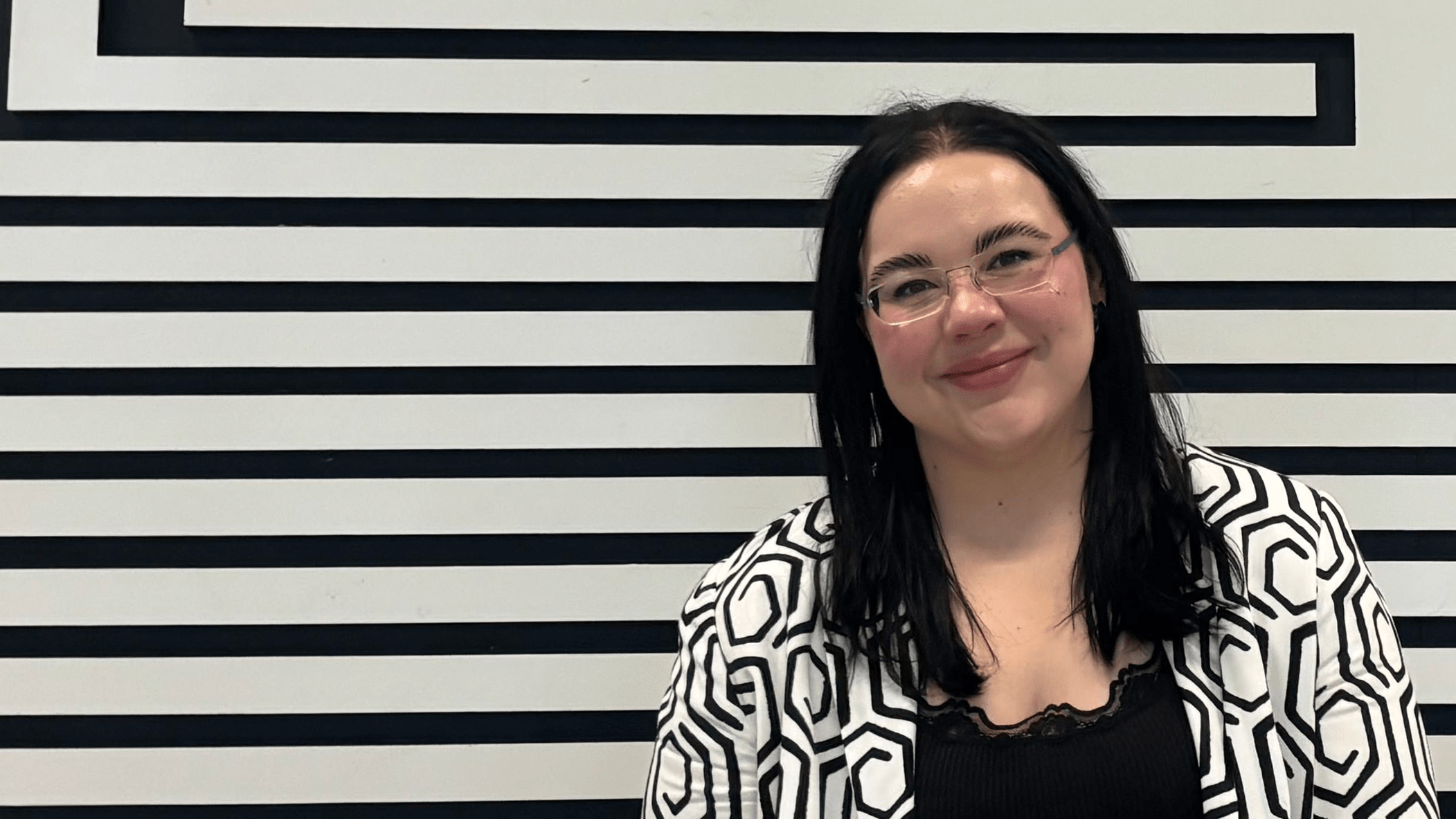 A woman with black hair and glasses posing in front of black and white art.