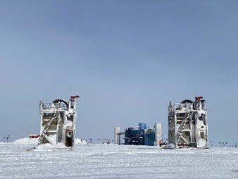 Two drilling towers set up at the Pole with the IceCube Lab seen between them in the background.