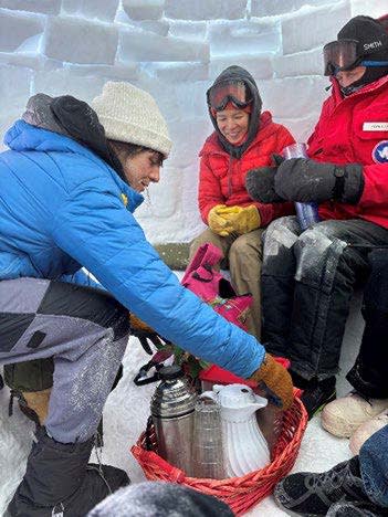 People serving and enjoying a hot beverage inside an igloo.