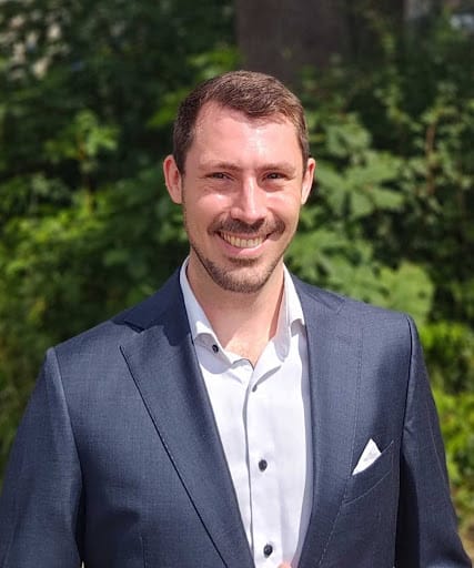 A headshot of a man in a suit smiling.