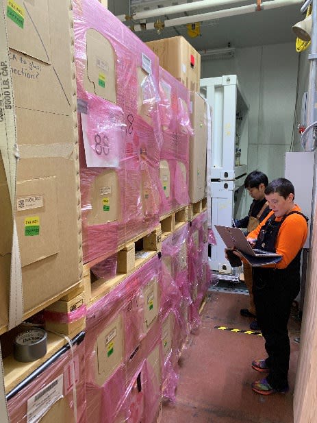 Two people holding laptops in front of tall stacks of boxes.