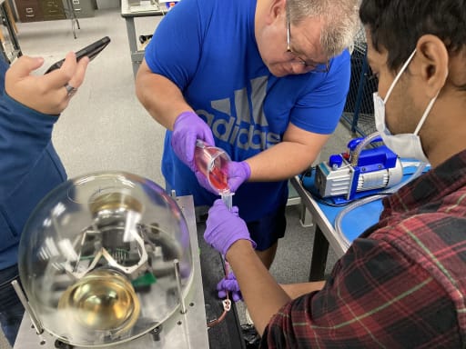 Close-up overhead of two people in lab pouring liquid into tube.