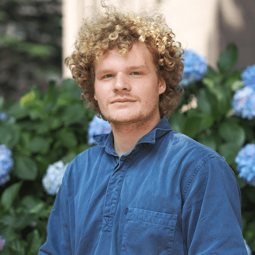A headshot of a man with a blue shirt and curly hair.
