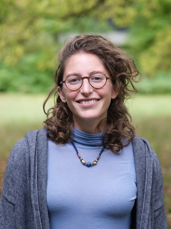 A headshot of a woman with a blue shirt wearing glasses.