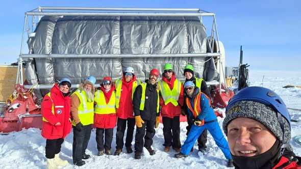 Group photo in front of large wrapped-up hose reel.