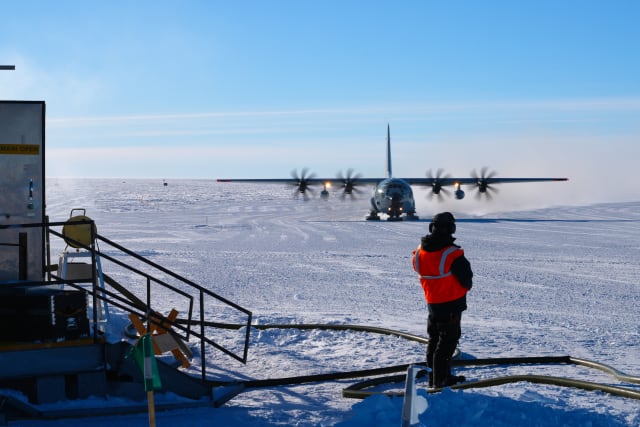 An aircraft marshaller seen from behind, waiting as large turboprop plane approaches.
