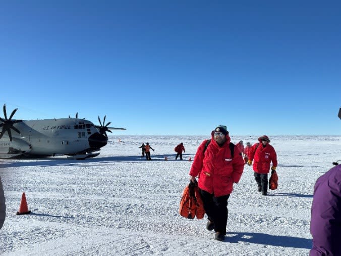 People in red parkas walking forward, away from parked plane behind them.