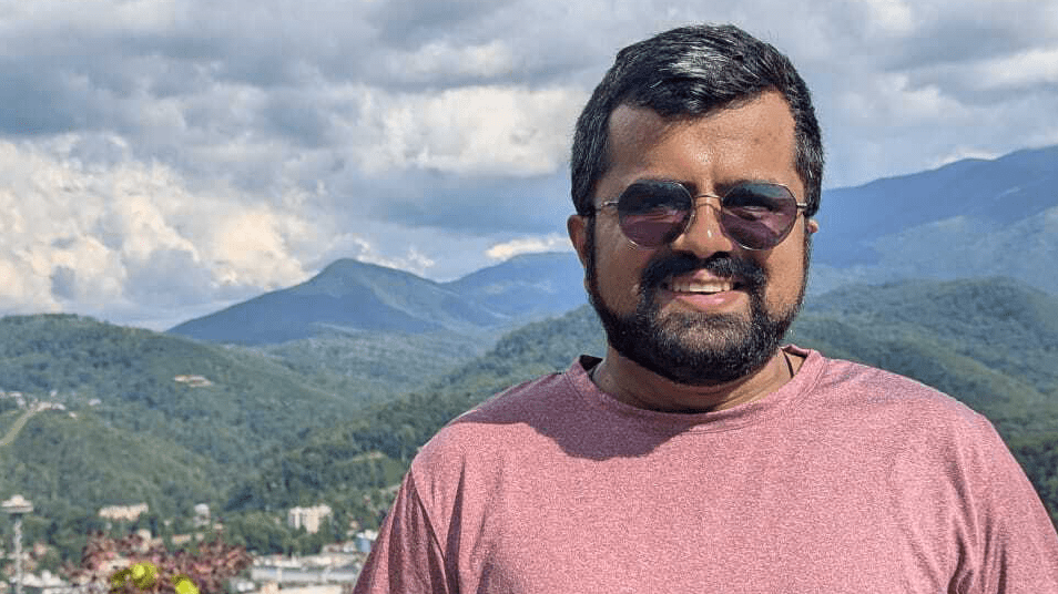 A man posing for a photo with mountains and trees in the background.