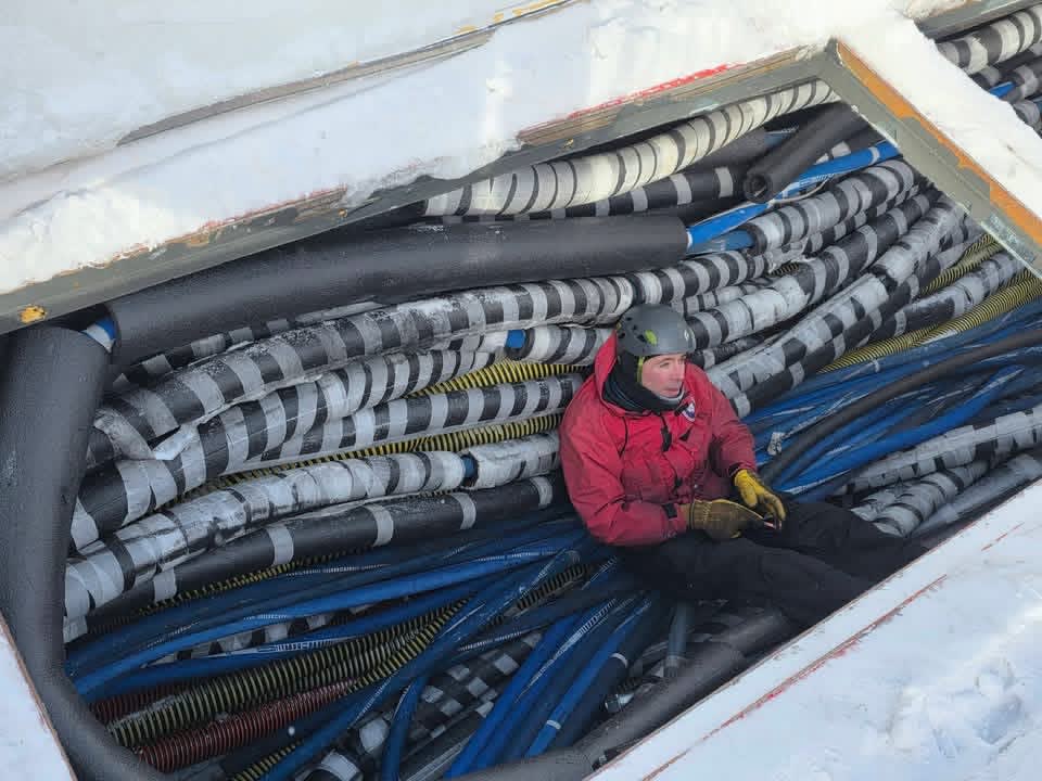Looking down at person resting on mass of coiled hose in undersurface storage tank.