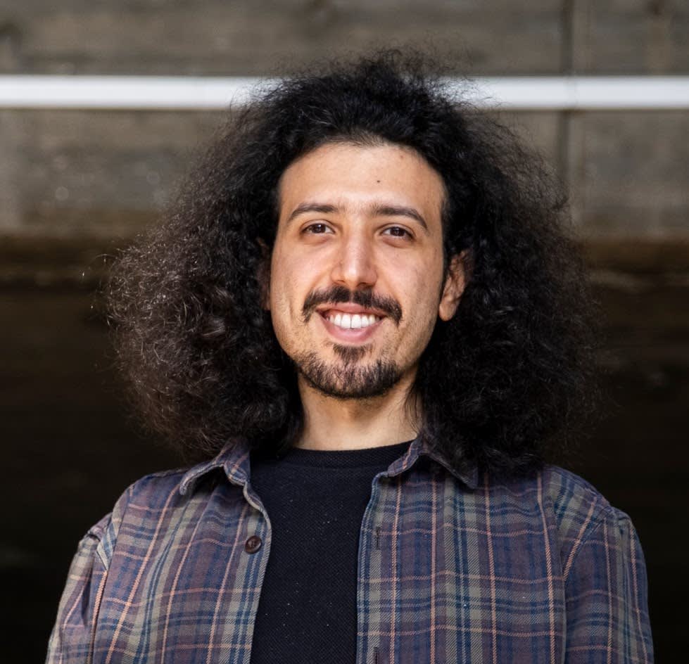 A man with a black afro smiling in a headshot.