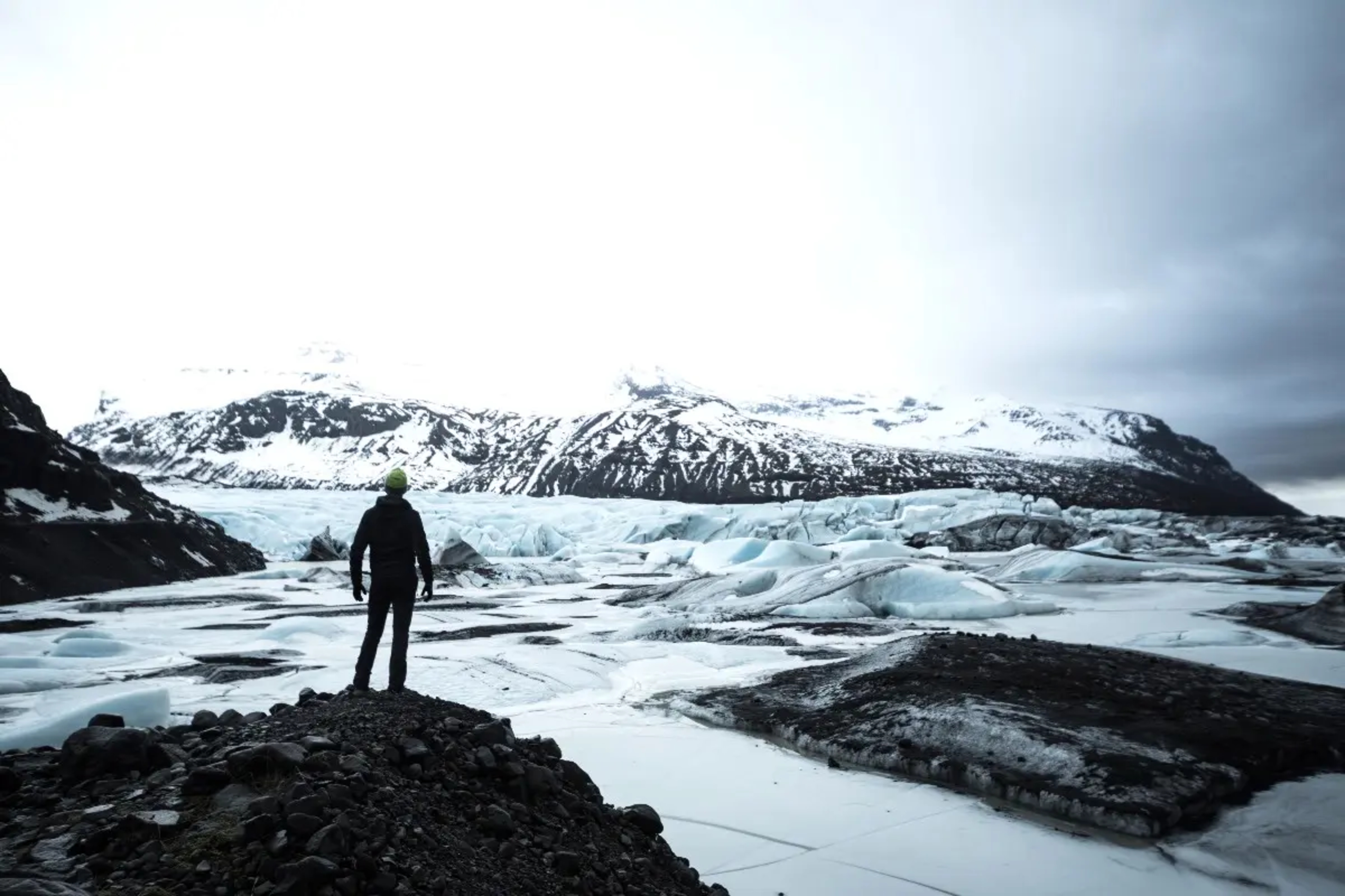 person standing on rock looking over glacier landscape and snowy mountains