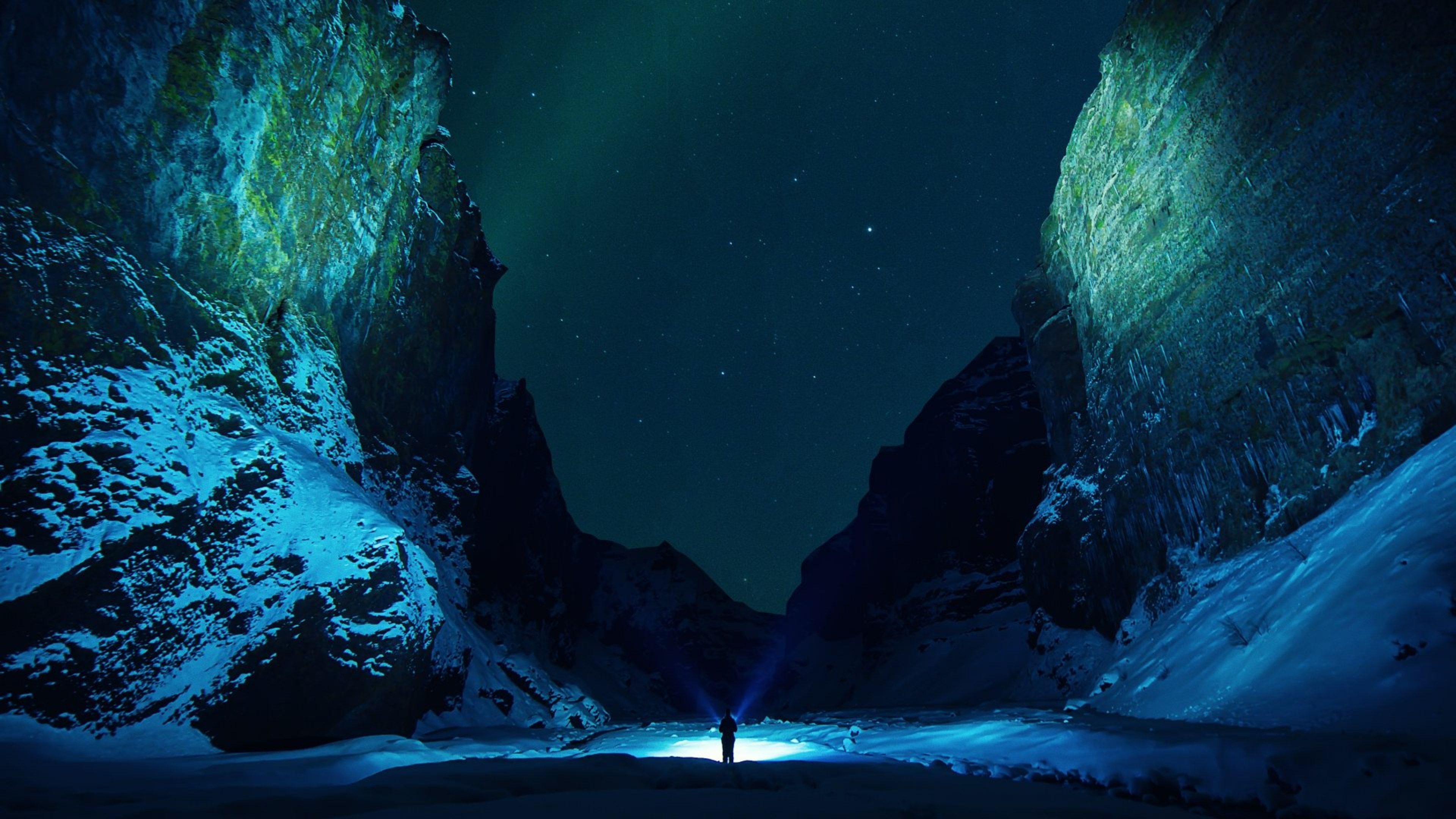 A man looking through Stakkholtsgjá gorge with the Northern Lights above