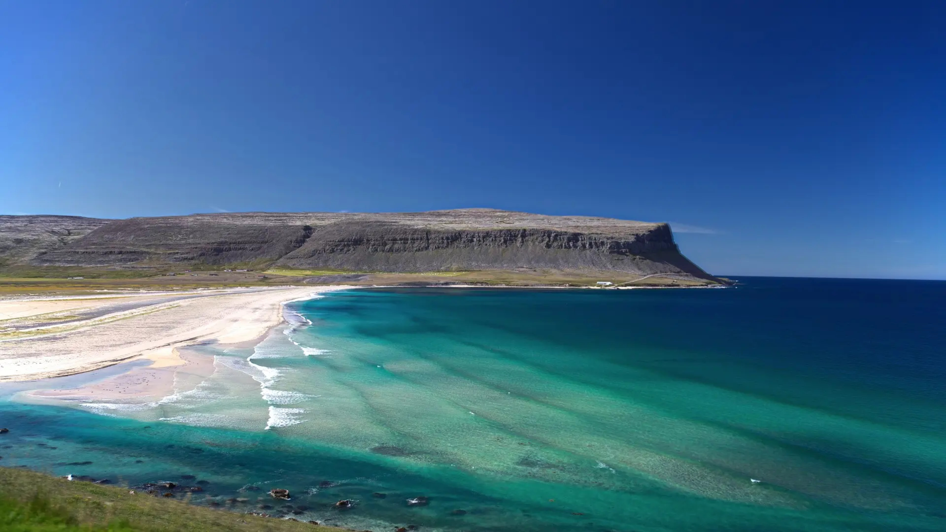 white sand beach with blue waters between dark mountains