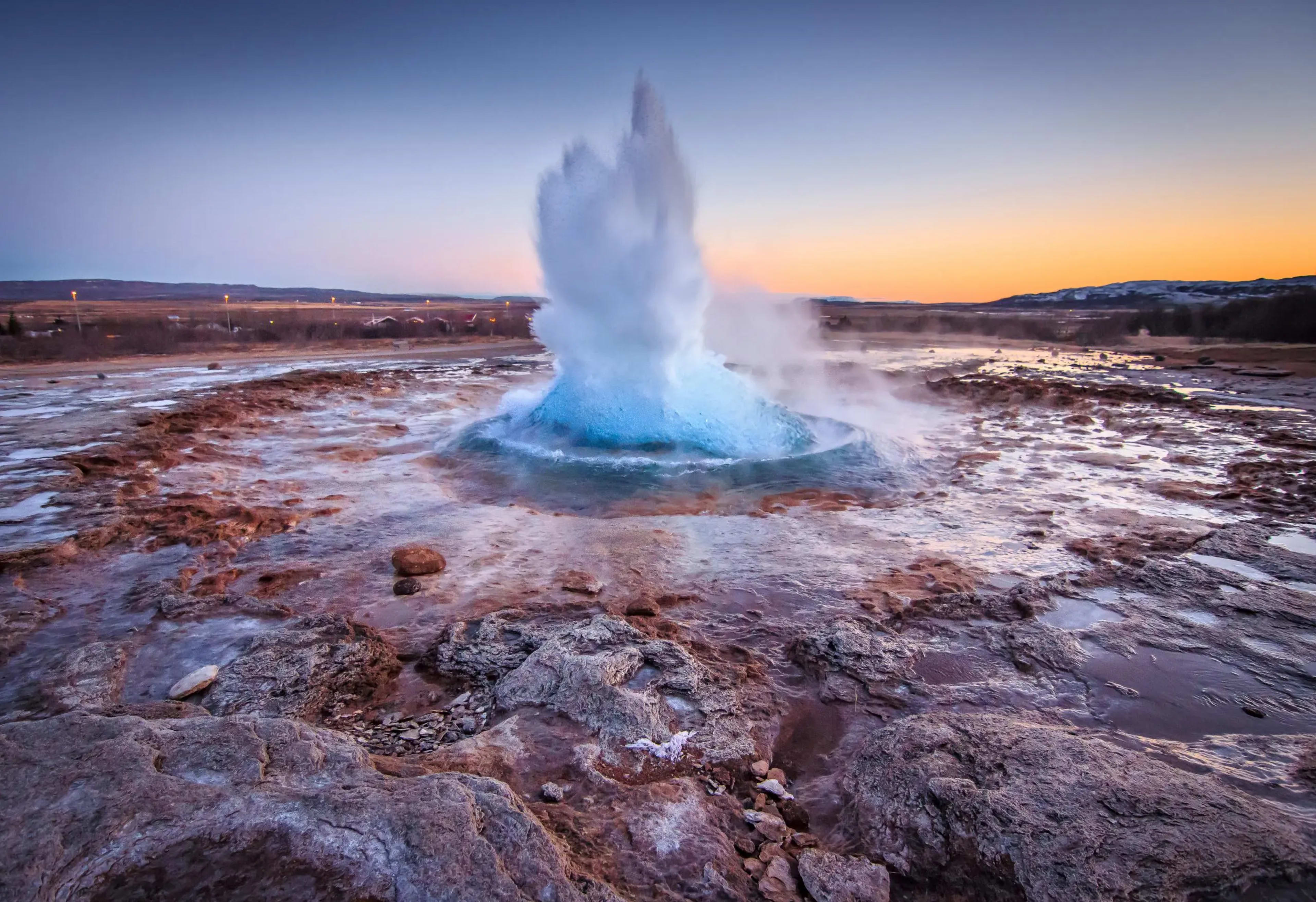 geyser erupting amidst rocky landscape with orange sunset