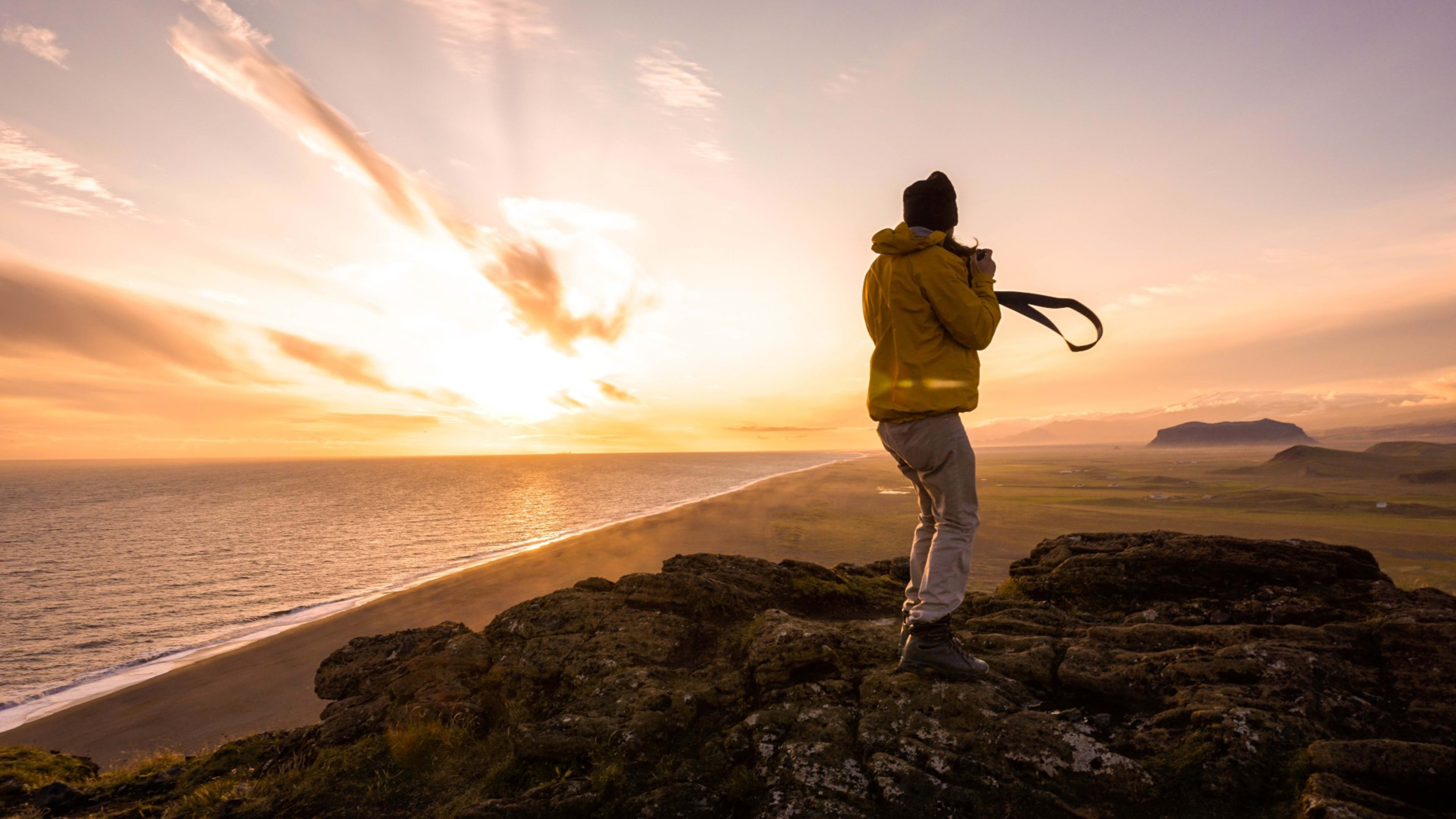 A woman holding a camera standing on a cliff with a sunset in the background