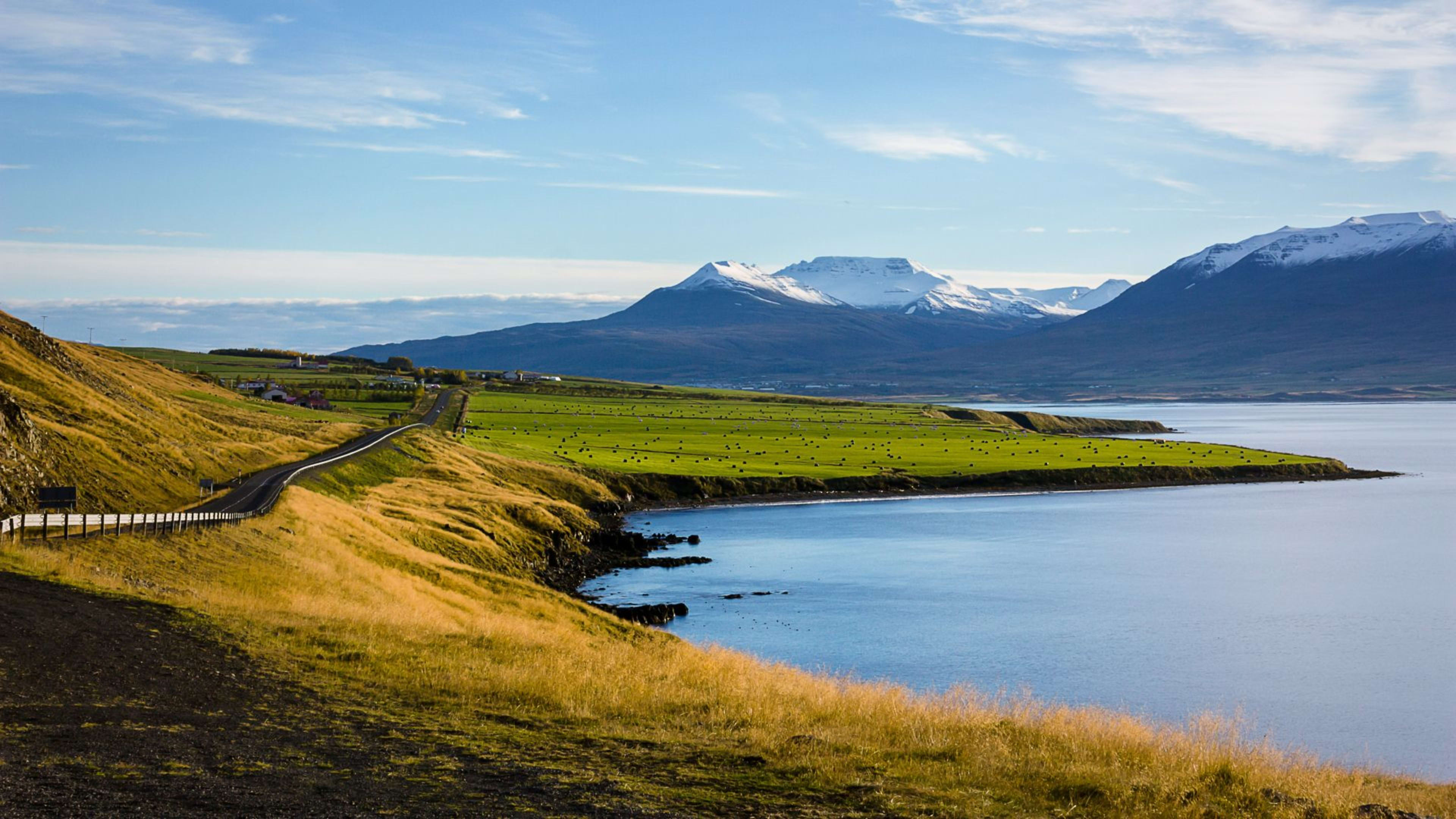 A road near Akureyri on a sunny day with snowcapped mountains in the distance