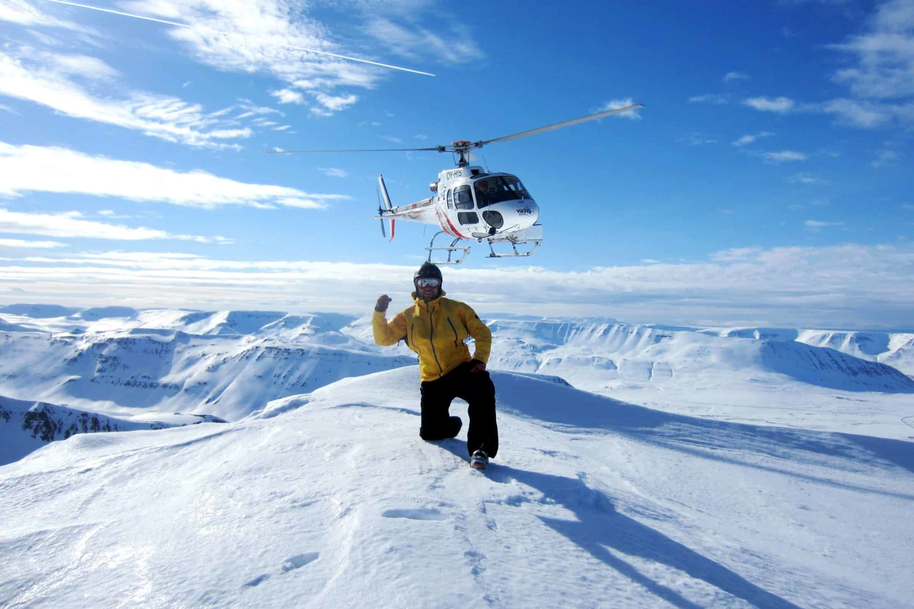 Man posing on a top of the mountain with helicopter in the background