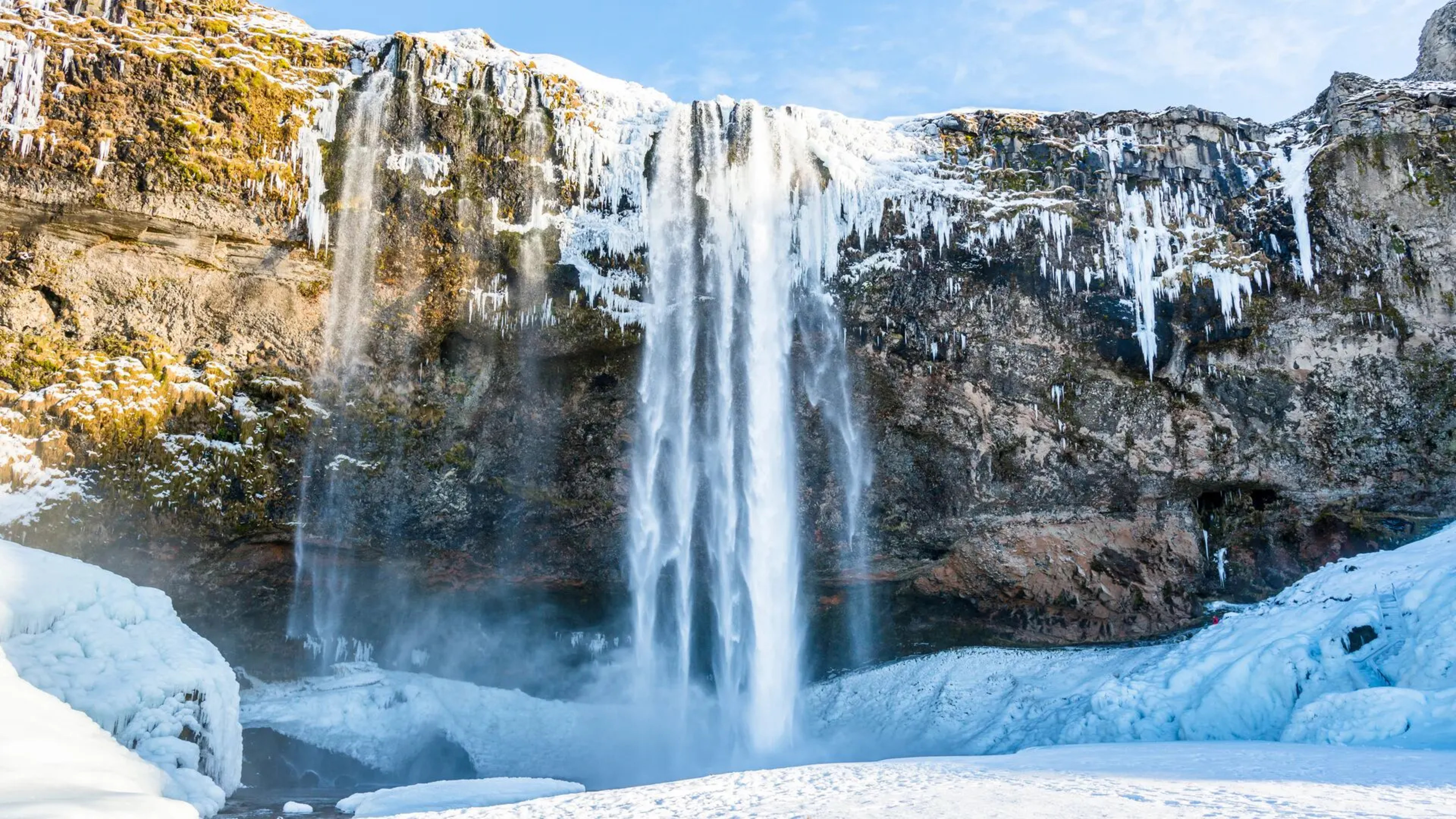 icicles and waterfall tumbling down rock face with snow on the ground