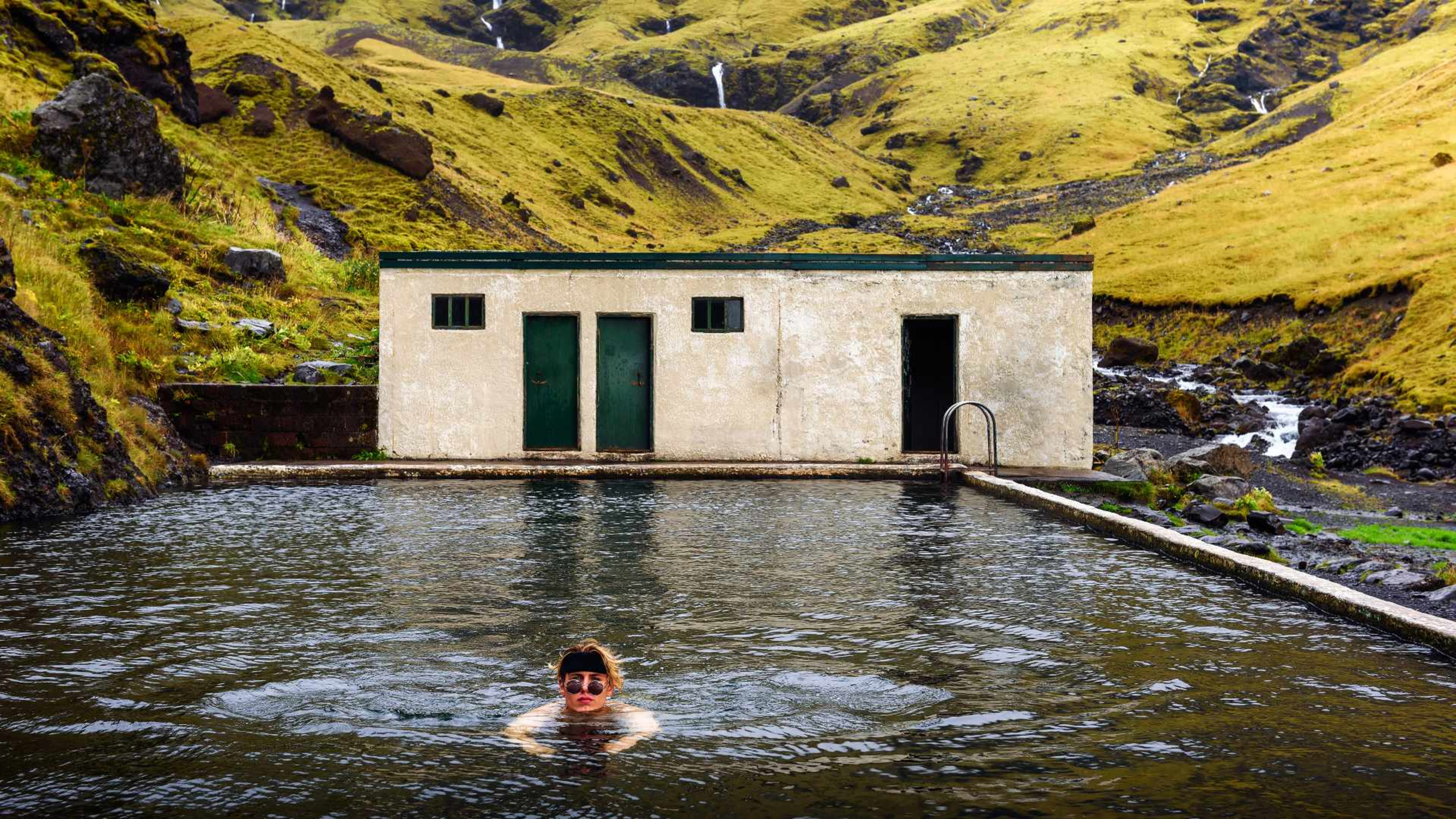 A woman with sunglasses swims in the Seljavallalaug pool in South Iceland