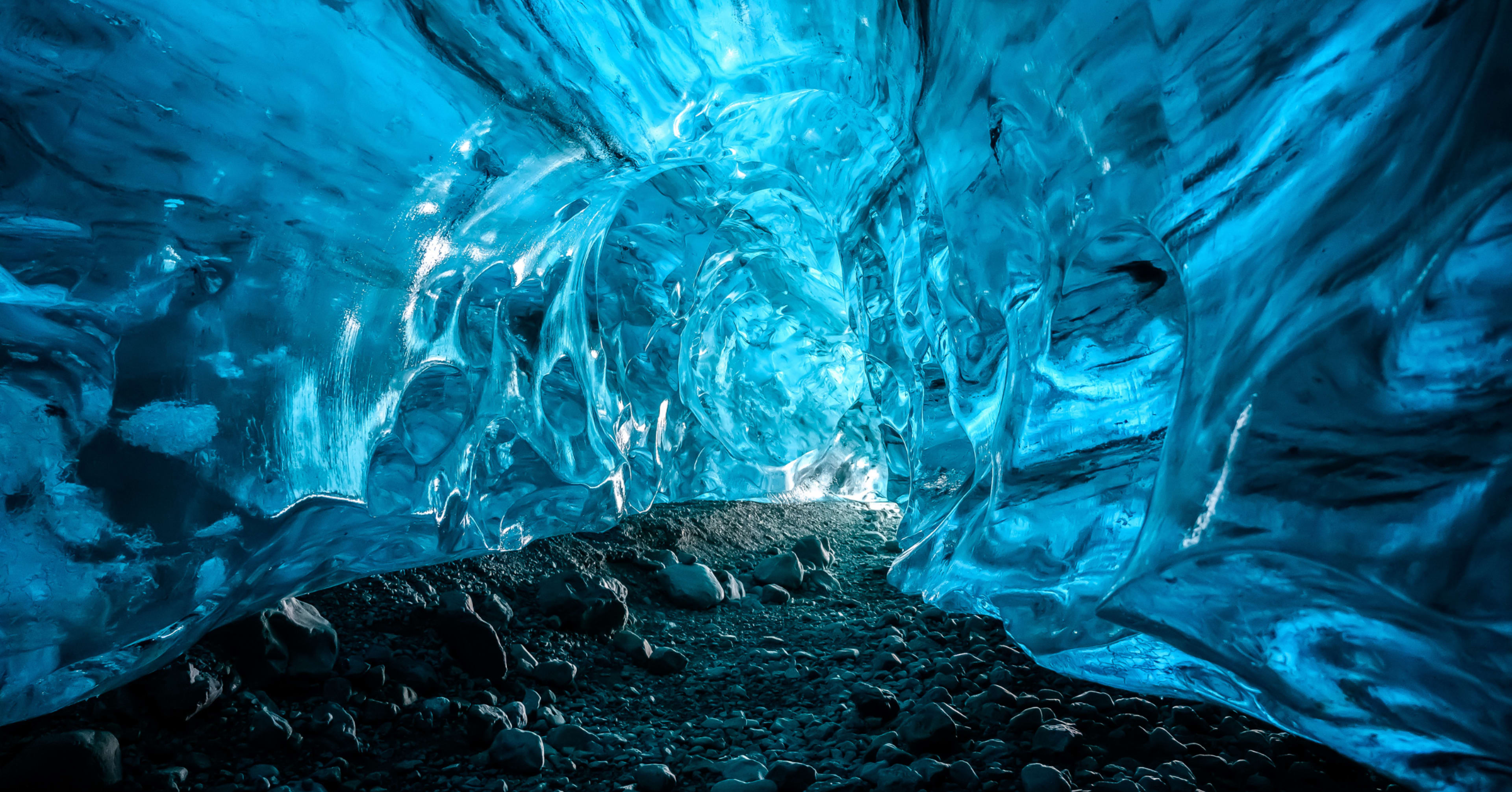 Vivid blue ice walls and rocky floor inside a natural ice cave in Iceland, showcasing translucent glacier textures.