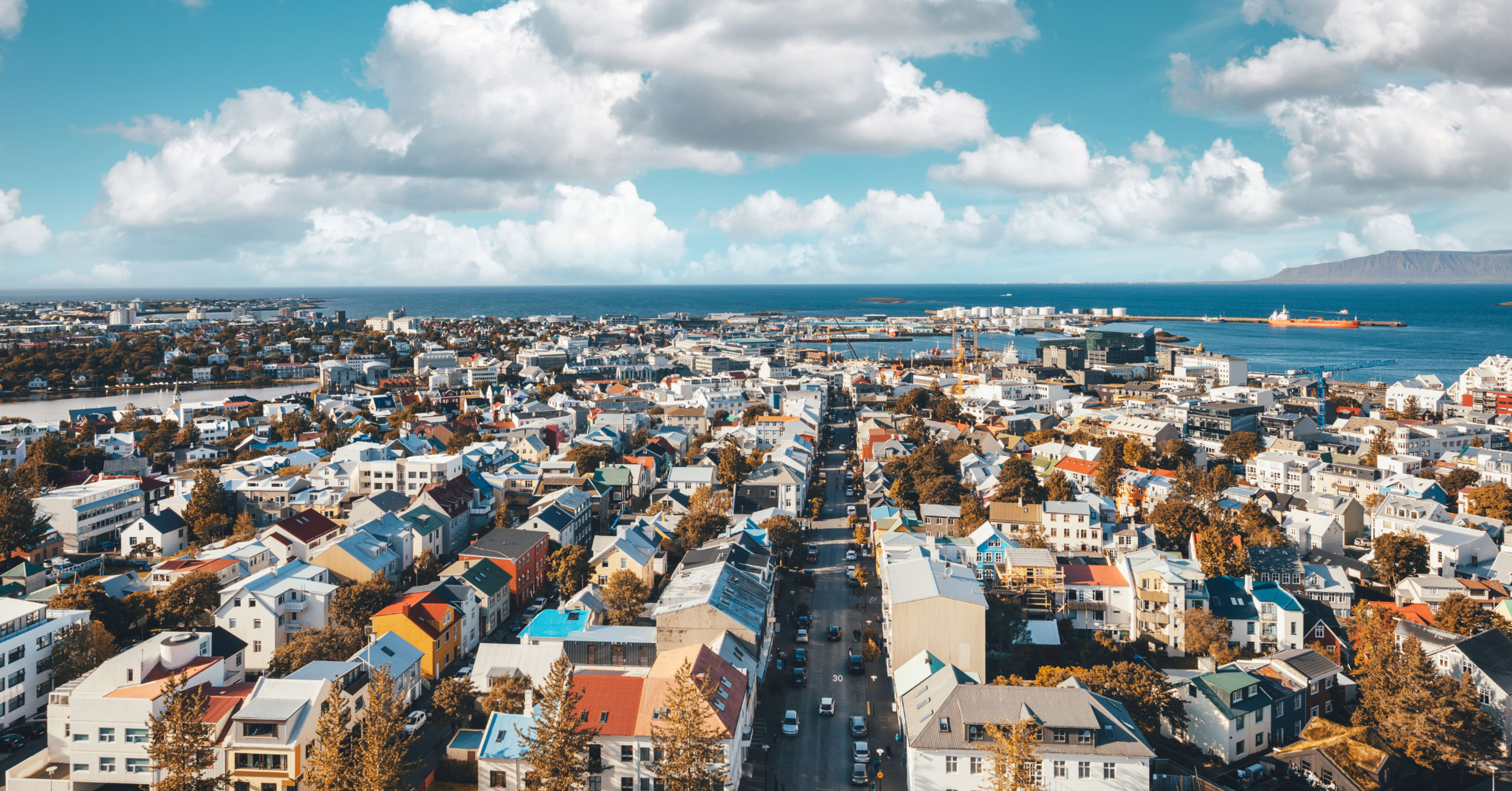  Panoramic aerial view of Reykjavík, Iceland, with colorful rooftops, the ocean, and Mount Esja in the distance.