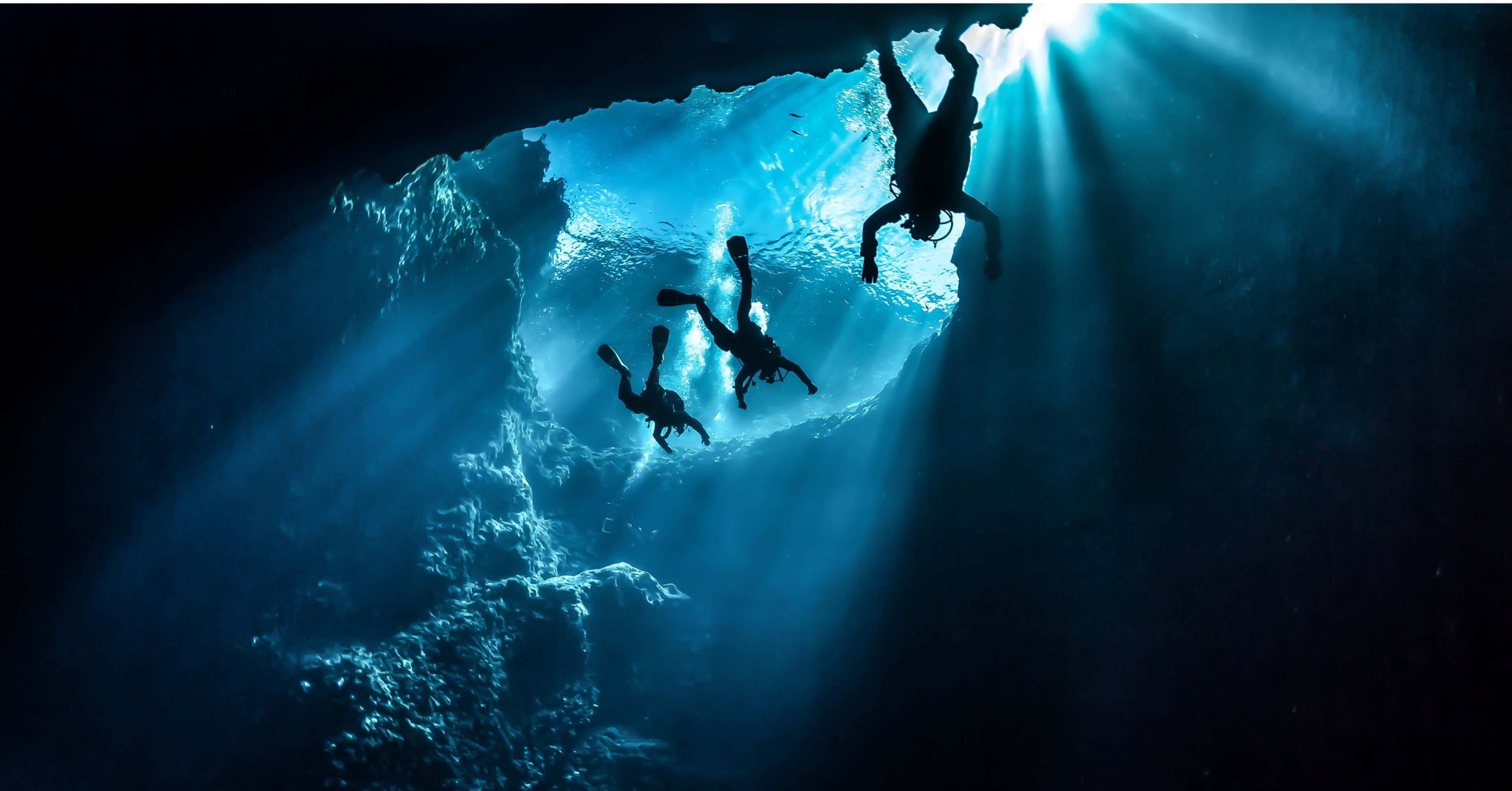Silhouetted divers exploring the crystal-clear blue depths of the Silfra fissure
