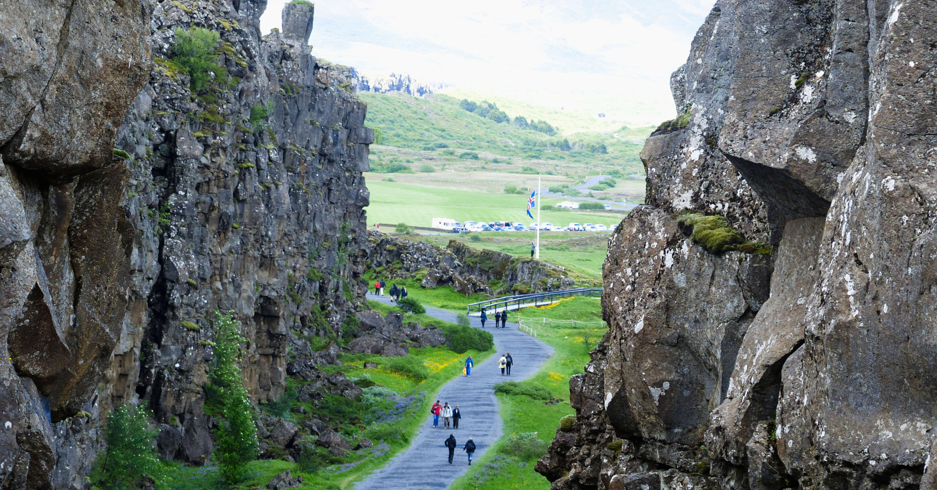 Paved trail winding between tall basalt cliffs with the Icelandic flag in the distance