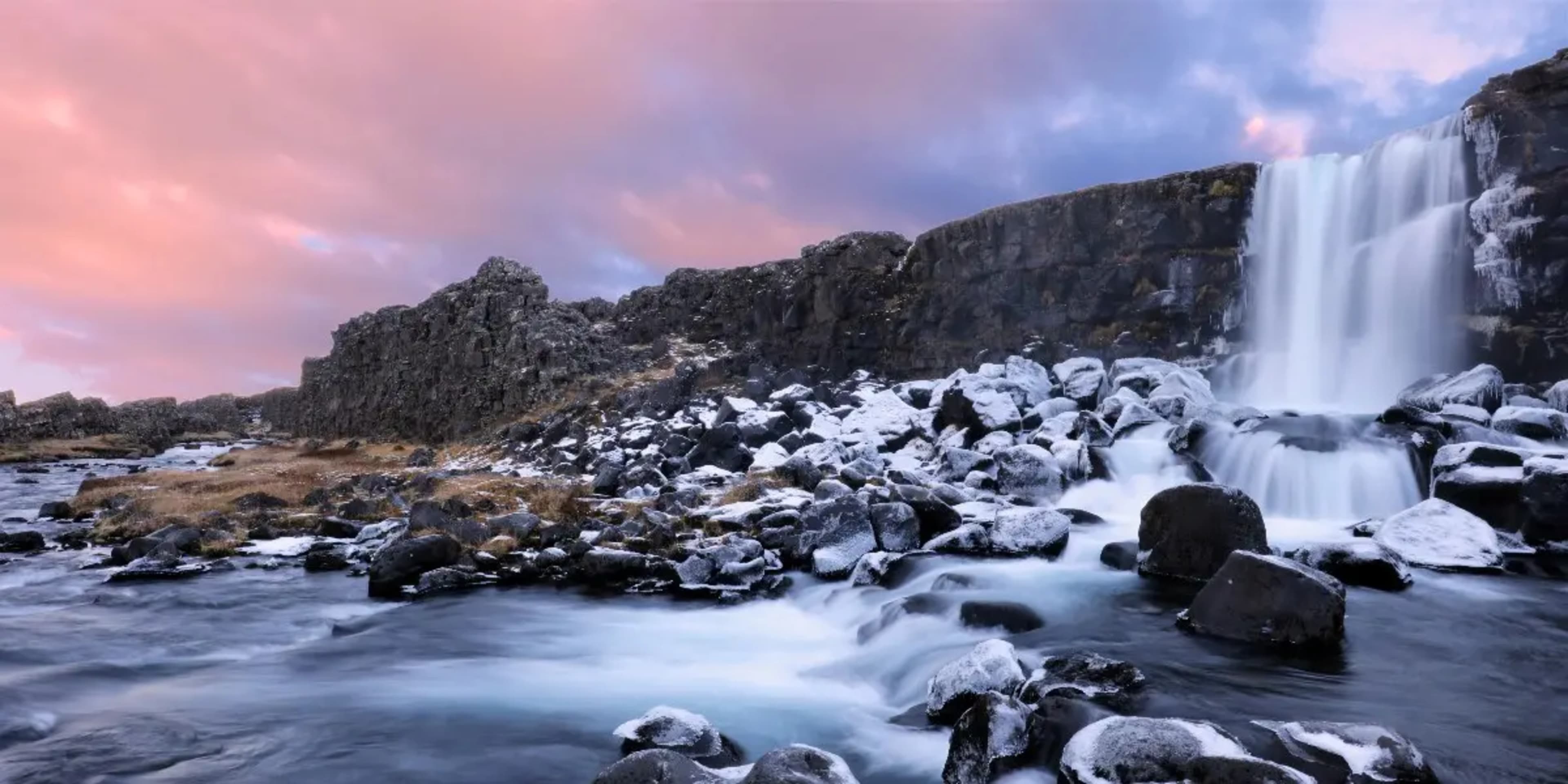 long exposure of waterfall on rocky river with pink sky of clouds