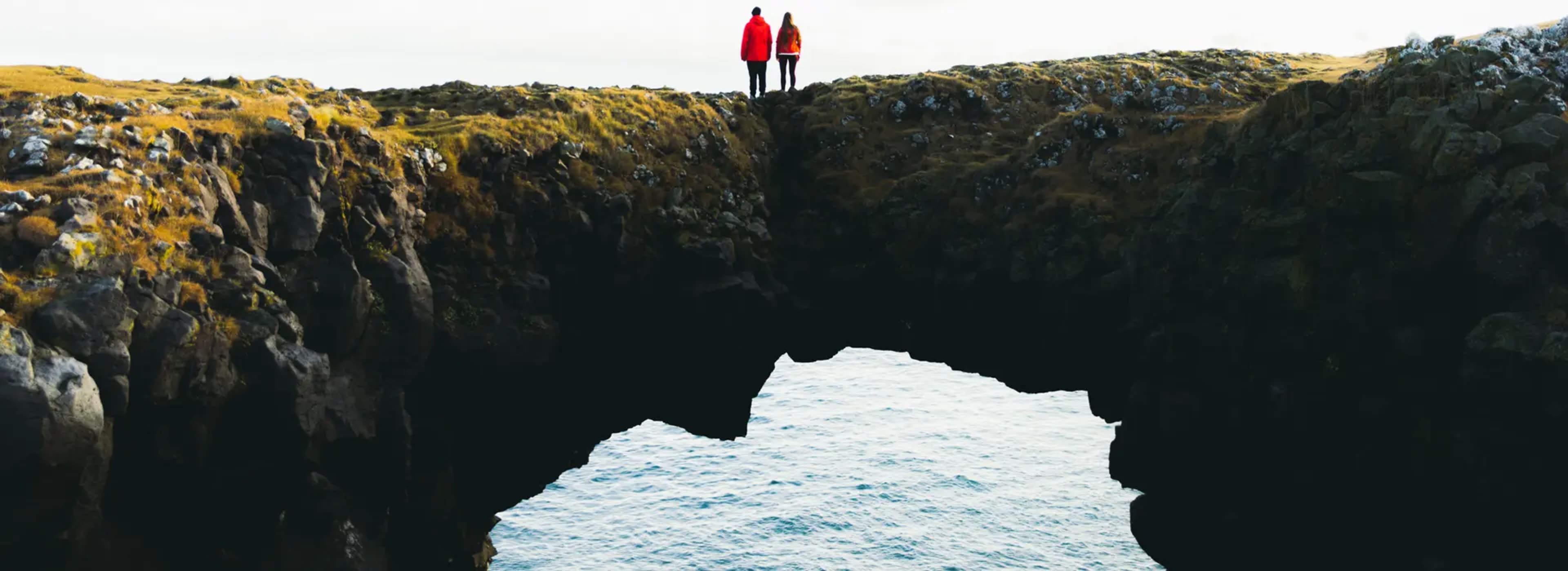 A couple standing in the middle of the Stone Bridge in Arnarstrapi